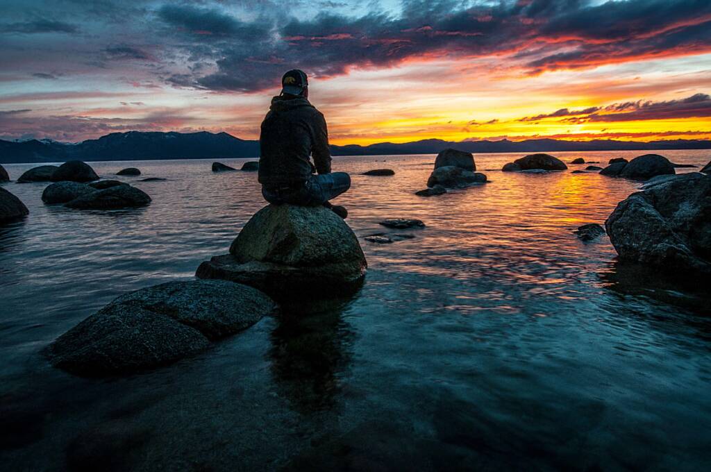 man sitting on rocks looking out over the water